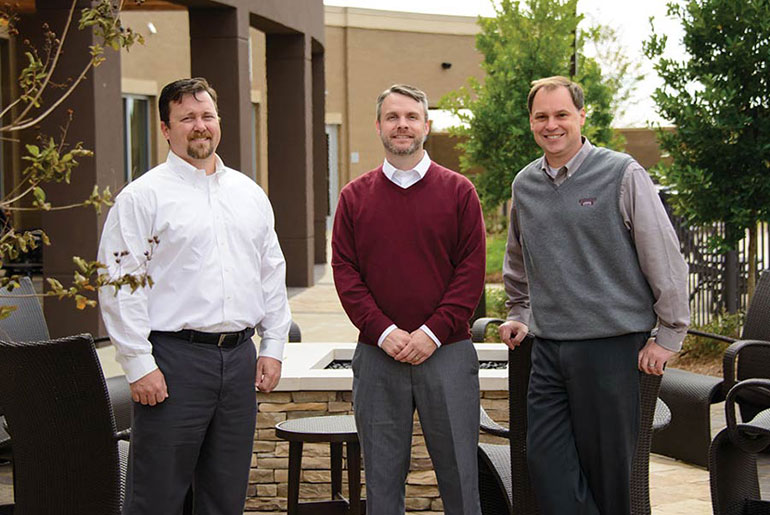 Three alumni pose outside landscape feature