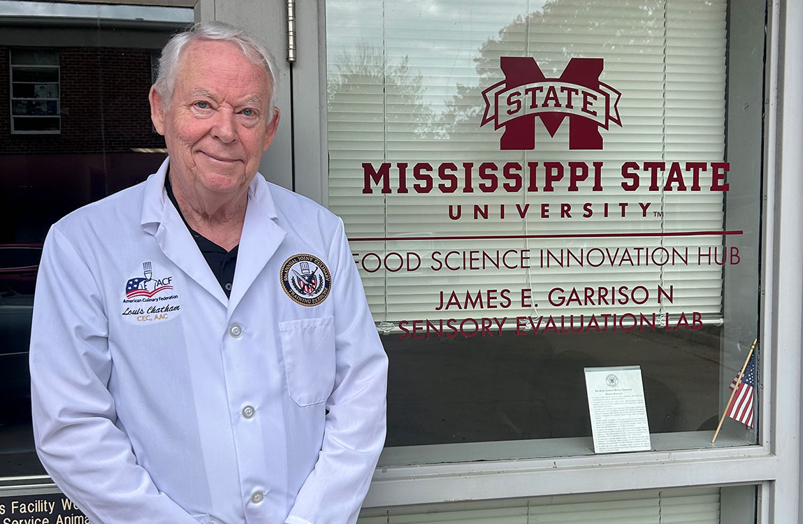 man in white lab coat standing in front of building with Mississippi State logo and Food Science Innovation Hub and James E. Garrison Sensory Evaluation Lab